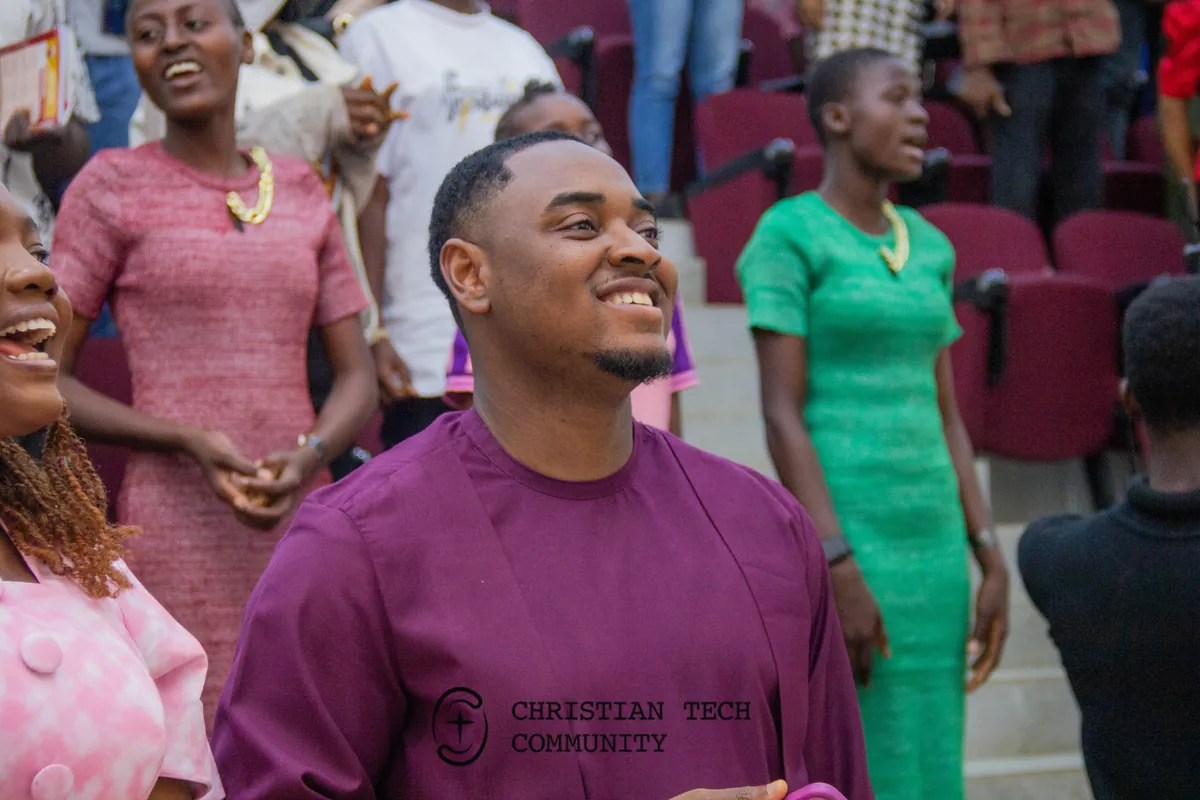 A man in a purple shirt smiles in the audience at CTC 1.0 while people around him laugh.